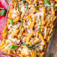 a casserole dish filled with pasta, cheese and spinach sprinkled with fresh basil