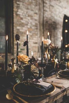 the table is set with candles, plates and napkins in front of an old brick wall