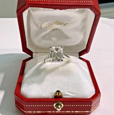 an open red box with a ring in it and a white cloth inside that says clicher