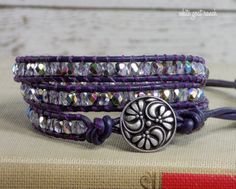 a purple leather bracelet with silver beads and a medallion on the clasp is sitting on top of a book