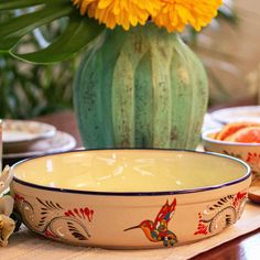 the bowl is sitting on the table next to the vase with yellow flowers in it