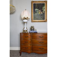 a painting hangs on the wall next to a dresser with a lamp and other items