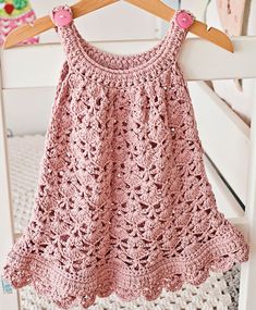 a pink crocheted top hanging on a wooden hanger next to a white chair