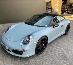 a blue sports car is parked in front of a building on a brick sidewalk with the roof down