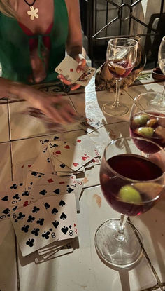 two women are playing cards at a table with wine glasses and card decks on it