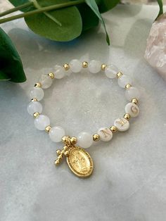 - Beautiful stretch catholic rosary bracelet made with white jade gemstone, pearl initials and 18k gold filled beads. This personalized rosary is adorned with cross charm and Blessed Virgin Mary medal. Bracelet is beaded on high quality stretch cord and secured.  - Rosary bracelet comes in a standard 6.75" size. If you need slightly smaller or larger, please contact me as adjustments may be made. - 8mm white jade beads - 8mm pearl shell initial beads - 4mm gold filled beads - Listing photos incl Spiritual White Name Bracelet With 8mm Beads, Elegant White Miraculous Medal Jewelry, Personalized White Spiritual Stretch Bracelet, White Miraculous Medal Spiritual Jewelry, Gold Bracelets With Round Beads For First Communion, Gold Spiritual Rosary Bracelet For First Communion, Spiritual Gold Rosary Bracelet For First Communion, Gold Rosary Bracelet For Baptism, Adjustable Rosary Bracelet With Round Beads For Baptism