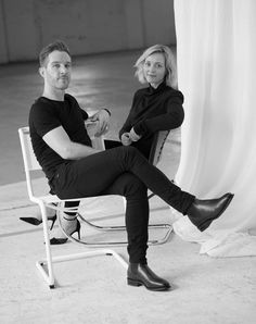 a man and woman sitting next to each other on a chair in front of a curtain