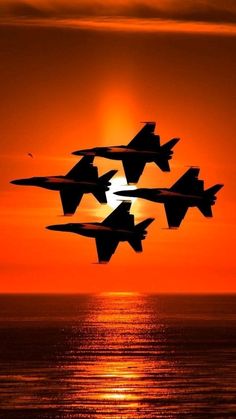 four fighter jets flying in formation over the ocean at sunset or sunrise with sun reflecting on water