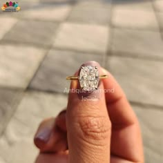 a woman's hand holding an engagement ring with a diamond in the middle, on a tile floor