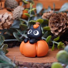 an orange and black cat figurine sitting on top of a wooden table next to pine cones