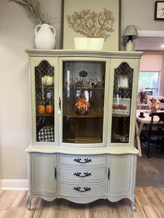 a white china cabinet with glass doors and drawers in a room filled with tables and chairs