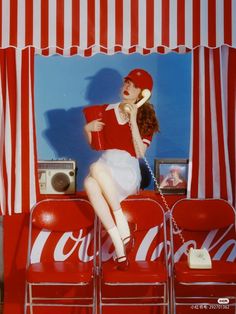 a woman sitting on top of a coca - cola chair talking on a phone with her legs crossed