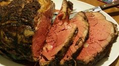 a large roast beef on a white plate with knife and fork next to the meat