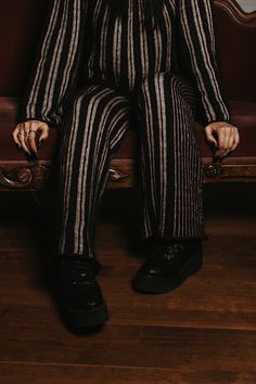 a man sitting on top of a brown couch wearing striped pants and black shoes with his hands in his pockets