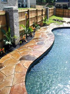 a backyard with a swimming pool and stone walkway leading up to the fenced in area