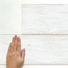 a person's hand on top of a white wood paneled flooring board