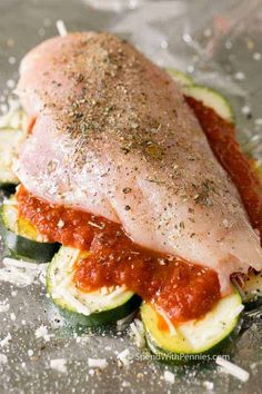 raw chicken breast on zucchini slices covered in marinara sauce and parmesan cheese