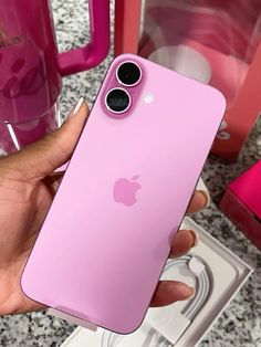 a person holding an iphone in their hand next to some cups and pink items on the table