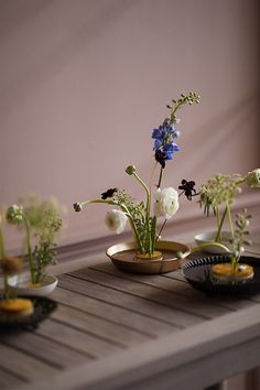 three small vases filled with flowers sitting on top of a wooden table next to each other