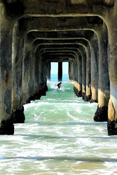 black and white photograph of a person surfing under a pier