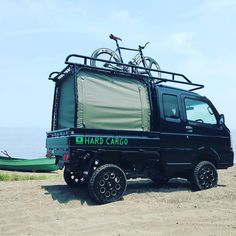 a black truck parked on top of a sandy beach next to the ocean with a bike mounted on it's roof