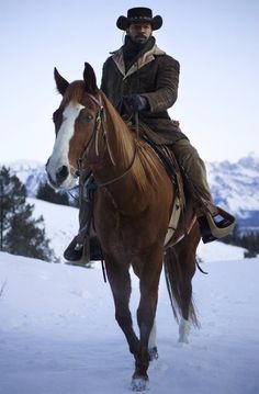 a man riding on the back of a brown and white horse in snow covered field