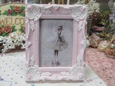 a pink frame with a ballerina doll in it on a table next to other items