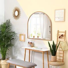 a white chair sitting next to a wooden desk in front of a mirror and potted plant