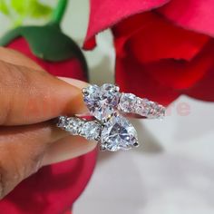 a woman's hand holding two diamond rings in front of a red rose flower