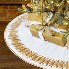 a christmas tree with gold presents under it on a white tablecloth covered placemat