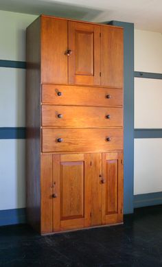 a tall wooden cabinet sitting on top of a black floor next to a white wall