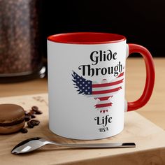 a red and white coffee mug sitting on top of a wooden table next to a cookie