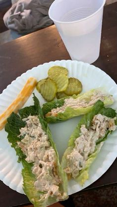 a paper plate topped with lettuce covered in tuna and pickles next to a cup of water