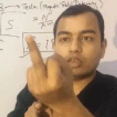 a man is making the v sign with his fingers while standing in front of a whiteboard