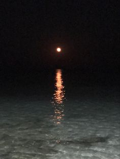 a full moon is seen over the ocean at night time with only one light visible