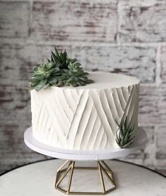 a white cake with succulents on top sitting on a stand next to a brick wall