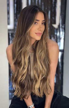 a woman with long, wavy hair sitting in front of a window and looking at the camera