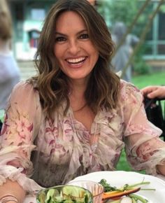 a woman sitting at a table with food in front of her and smiling for the camera