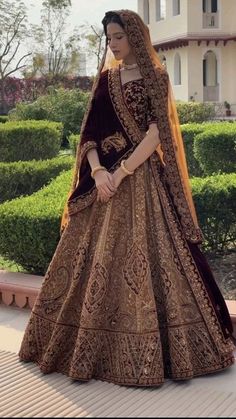 a woman in a brown and gold bridal gown standing on a sidewalk with bushes behind her