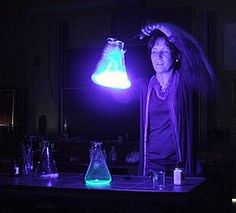 a woman standing in front of a table filled with flasks and beakles