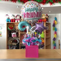 a birthday balloon sitting on top of a table next to a pink gift box filled with balloons