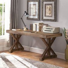 a wooden desk with books on it in front of two framed pictures and a lamp