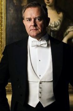 an older man in a tuxedo and bow tie standing next to a painting