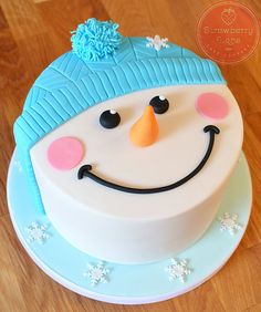 a frosted cake decorated with a smiling snowman face on a wooden table top