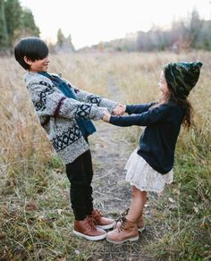 two young children holding hands and standing in tall grass with trees in the back ground