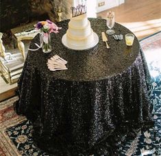 a table topped with a white cake on top of a black table cloth next to a fireplace