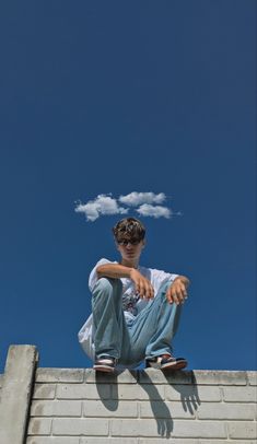 a young man sitting on top of a brick wall