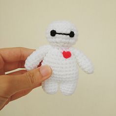 a hand holding a small white crocheted stuffed animal with a red heart on it's chest