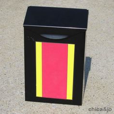 a black trash can with pink and yellow stripes on the side, sitting on concrete