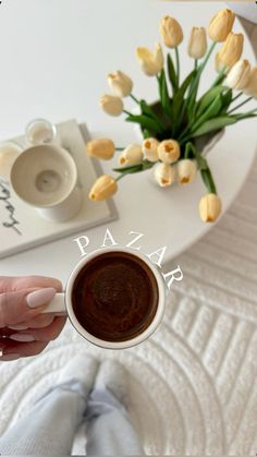 a person holding a cup of coffee in front of a table with flowers on it